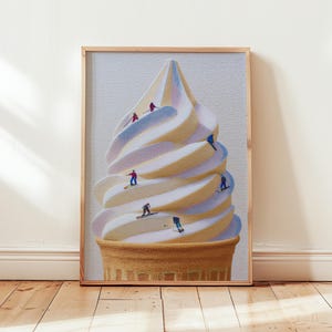 May include: A framed art print featuring a whimsical illustration of a soft-serve ice cream cone with tiny skiers and snowboarders. The cone is a light brown color, and the ice cream is swirled with white, yellow, and light blue. The artwork is displayed on a wooden floor.