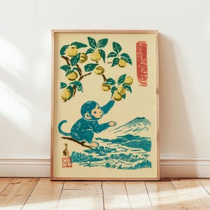May include: A framed print featuring a blue monkey reaching for yellow fruit on a tree branch. The print has a mountain and landscape in the background, with a red vertical rectangle on the right. The artwork is in a vintage Japanese style.