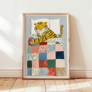 May include: A framed art print depicting a sleeping tiger with yellow and black stripes, on a bed with a patchwork quilt. The quilt is made of various colourful fabric squares. The background is a light blue.