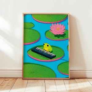 Op de afbeelding: Een ingelijste kunstdruk met een cartoonkikker die keyboard speelt op een waterlelieblad. De kikker is limoengroen met grote zwarte ogen. De waterleliebladeren zijn groen met roze randen en drijven op een blauwe vijver. Een roze lotusbloem is ook aanwezig.