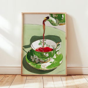 May include: A framed painting depicts a green teacup and saucer with white floral designs. Dark liquid pours from a green teapot into the teacup, which sits on a green table. The artwork is set against a neutral background.