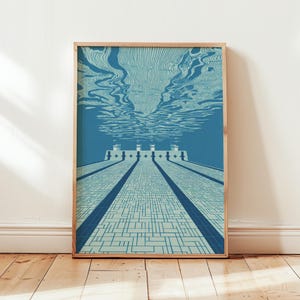 May include: A framed art print featuring an underwater view of a swimming pool. The artwork uses shades of blue and white to depict the pool's lanes, tiled bottom, and the water's surface. The print is in a light wooden frame.