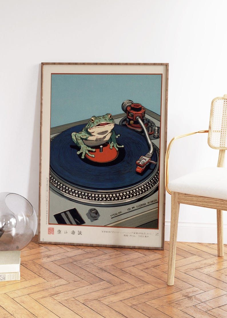 May include: Framed art print featuring a green frog on a blue record, positioned on a silver turntable. The artwork has a vintage aesthetic with a red tone and Japanese text at the bottom. The background is light blue.