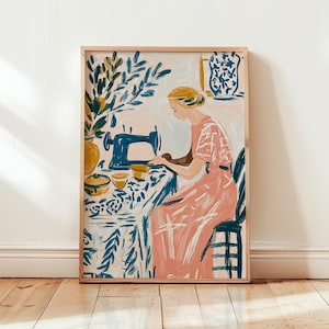 Puede incluir: Impresión artística enmarcada que representa a una mujer cosiendo. La obra de arte utiliza rosa, azul y amarillo. Una máquina de coser azul está sobre una mesa con una tela estampada. La mujer lleva un vestido rosa.