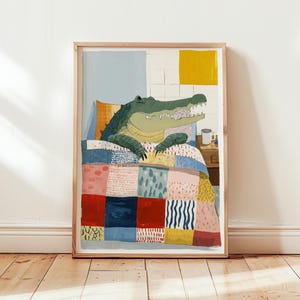 Pode incluir: Uma impressão de arte emoldurada com um jacaré verde na cama sob um edredom de retalhos colorido. O jacaré está descansando em um travesseiro com um padrão laranja e amarelo. Uma pequena mesa de cabeceira com uma caneca está ao lado da cama.