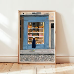 Könnte beinhalten: Ein Kunstdruck einer Bäckerei mit blauer Fassade und einer Auslage von Backwaren. Eine Person in einem dunklen Mantel und Hut steht vor dem Geschäft. Das Kunstwerk ist in einem hellen Holzrahmen gerahmt.
