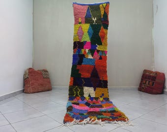 Puede incluir: Una alfombra marroquí colorida con patrones geométricos en tonos de rojo, azul, verde, amarillo y rosa. La alfombra está tejida a mano y tiene flecos en la parte inferior.