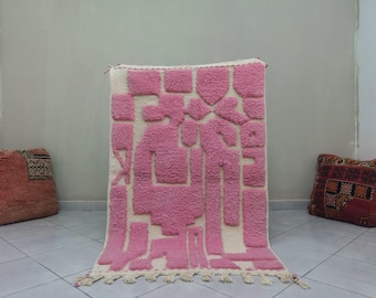 May include: A pink and white geometric patterned rug with fringe. The rug has a modern design with abstract shapes.