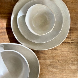 May include: Three ceramic bowls in various sizes, all in a light beige color. The bowls are nested together, with the smallest bowl in the center.