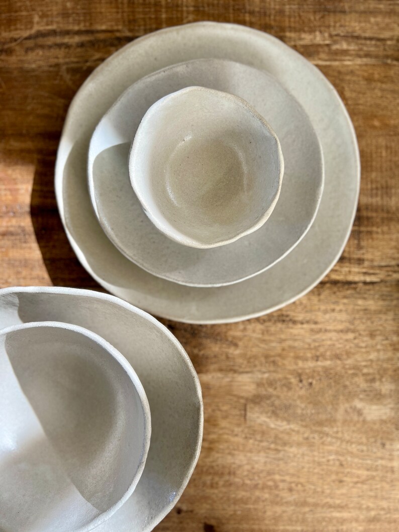 May include: Three ceramic bowls in various sizes, all in a light beige color. The bowls are nested together, with the smallest bowl in the center.