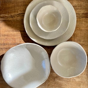 May include: Set of four ceramic bowls in a light beige color. The bowls are of varying sizes and have a slightly textured surface.