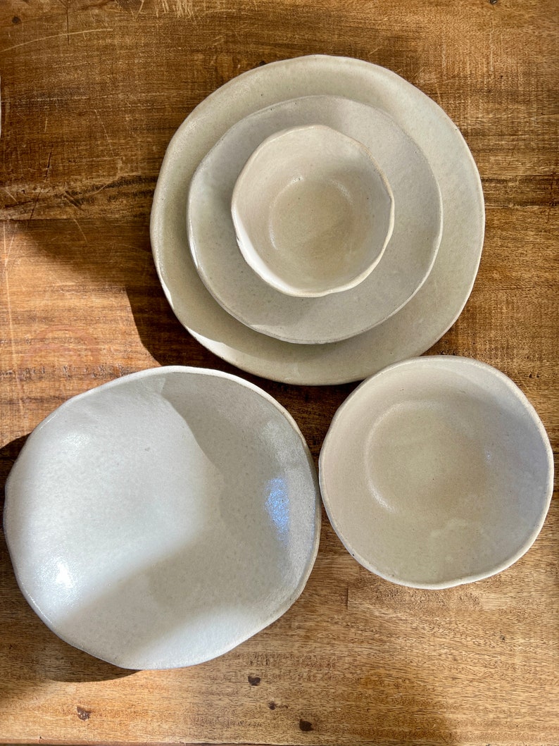 May include: Set of four ceramic bowls in a light beige color. The bowls are of varying sizes and have a slightly textured surface.