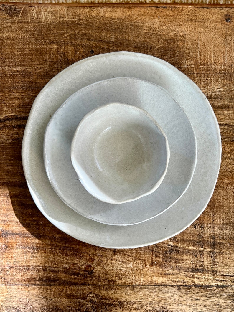 May include: Three ceramic bowls in various sizes, nested together. The bowls are a light gray color with a slightly textured surface.