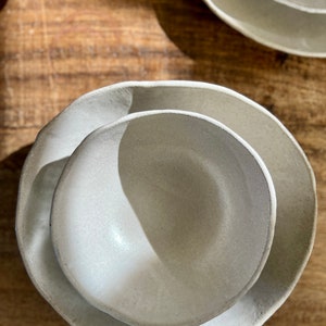 May include: Two white ceramic bowls, one nested inside the other. The bowls have a slightly textured surface and a rounded shape.