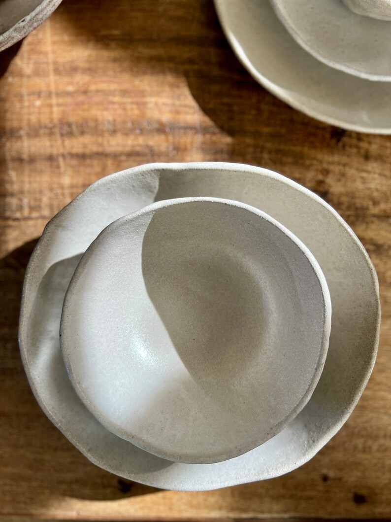 May include: Two white ceramic bowls, one nested inside the other. The bowls have a slightly textured surface and a rounded shape.