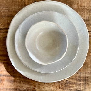 May include: Three ceramic bowls, nested together, in a light beige color. The bowls are handmade and have a slightly irregular shape.