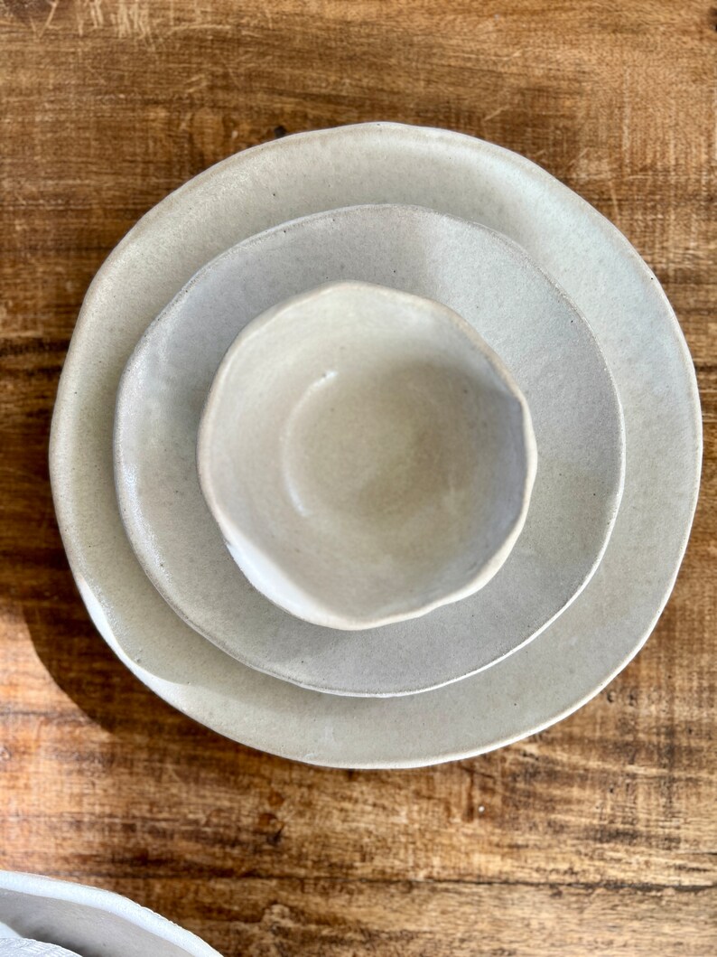 May include: Three ceramic bowls, nested together, in a light beige color. The bowls are handmade and have a slightly irregular shape.