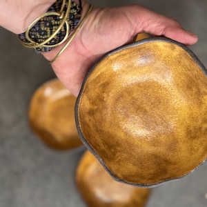 Peut inclure: Un ensemble de trois petits bols en céramique faits à la main avec une finition rustique, inégale et légèrement texturée. Les bols sont d'une couleur jaune foncé avec un bord brun foncé.