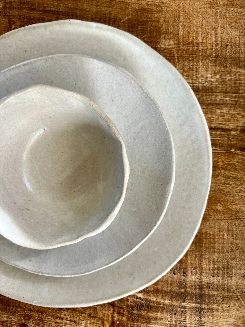 May include: Three ceramic bowls in various sizes, all in a light beige color, with a slightly textured surface. The bowls are stacked on top of each other, with the largest bowl on the bottom and the smallest bowl on top.