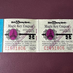 以下が含まれることがあります： ウォルト・ディズニー・ワールドのマジックキークーポン2枚。各クーポンには、楕円の中に城があるキーのデザインが施されています。「Good for One Admission」と「C1691806」の文字があります。クーポンには青色のミシン目が入っています。