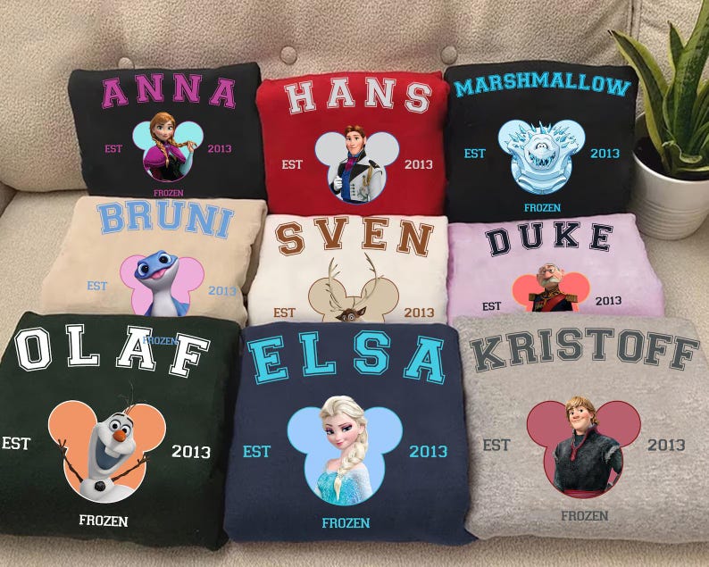 May include: A collection of sweatshirts in various colors, each featuring a character from the movie "Frozen". The sweatshirts display character names like Anna, Hans, and Olaf, along with the year "2013" and the word "Frozen".