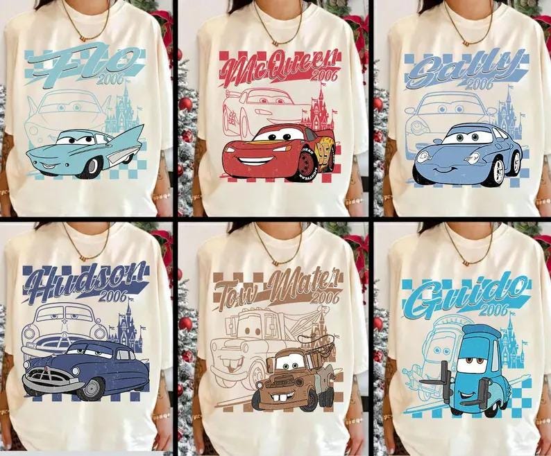 Op de afbeelding: Cr&egrave;mekleurige T-shirts met verschillende personages uit de animatiefilm "Cars". Elk shirt toont de naam van een ander personage, het jaar 2006 en een illustratie van de auto van het personage in blauw, rood en bruin.