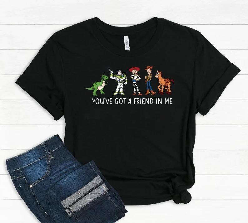 May include: Black t-shirt featuring a graphic of cartoon characters from the movie Toy Story. The characters include a green dinosaur, Buzz Lightyear, Jessie, Woody, and a horse. The text "YOU'VE GOT A FRIEND IN ME" is printed below the characters.