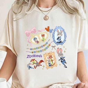 May include: A cream-coloured t-shirt with a design from the film "Zootopia." The design includes framed character portraits, the film's logo, and the phrase "Welcome to Zootopia." The shirt has short sleeves and is made of a soft material.