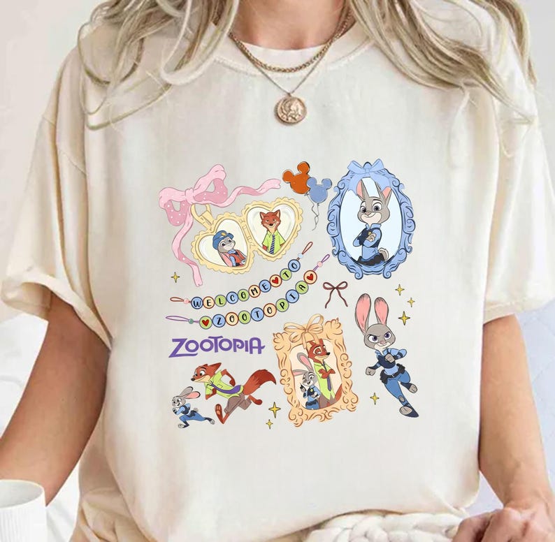 May include: A cream-coloured t-shirt with a design from the film "Zootopia." The design includes framed character portraits, the film's logo, and the phrase "Welcome to Zootopia." The shirt has short sleeves and is made of a soft material.