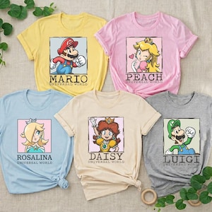 May include: Five short-sleeve t-shirts in yellow, pink, light blue, beige, and gray. Each shirt features a square graphic of a character from the Mario franchise with the text "UNIVERSAL WORLD" and the character's name: Mario, Peach, Rosalina, Daisy, or Luigi.