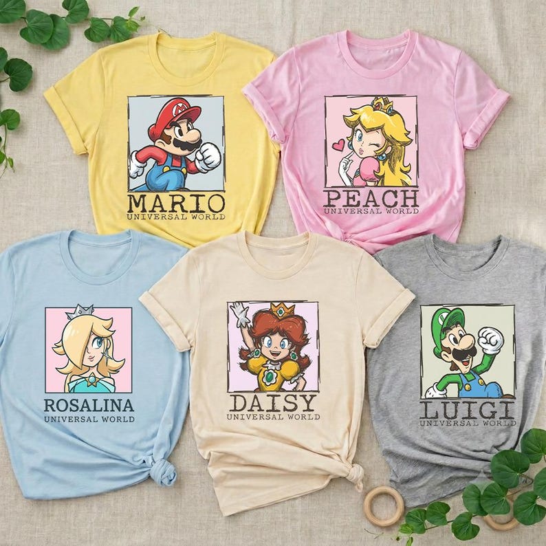 May include: Five short-sleeve t-shirts in yellow, pink, light blue, beige, and gray. Each shirt features a square graphic of a character from the Mario franchise with the text "UNIVERSAL WORLD" and the character's name: Mario, Peach, Rosalina, Daisy, or Luigi.
