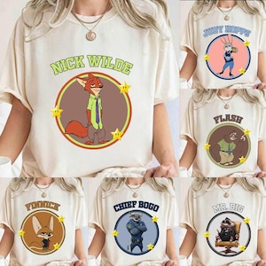 May include: Cream-colored t-shirts featuring cartoon characters from the movie Zootopia. Each shirt displays a character's name in a circle with a corresponding image and star accents. Characters include Nick Wilde, Judy Hopps, Flash, Finnick, Chief Bogo, and Mr. Big.