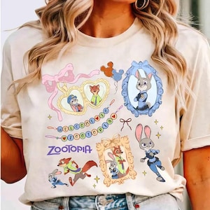 Puede incluir: Camiseta beige con ilustraciones coloridas de personajes de Zootopia. El dise&ntilde;o incluye retratos enmarcados de Judy Hopps y Nick Wilde, junto con el texto "WELCOME TO ZOOOTPIA".