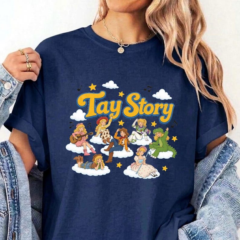 Pu&ograve; includere: Una t-shirt a maniche corte blu navy con una stampa grafica che riporta il testo giallo Tay Story. Il design raffigura diversi personaggi dei cartoni animati con capelli biondi e vari abiti, seduti su nuvole bianche tra stelle gialle.
