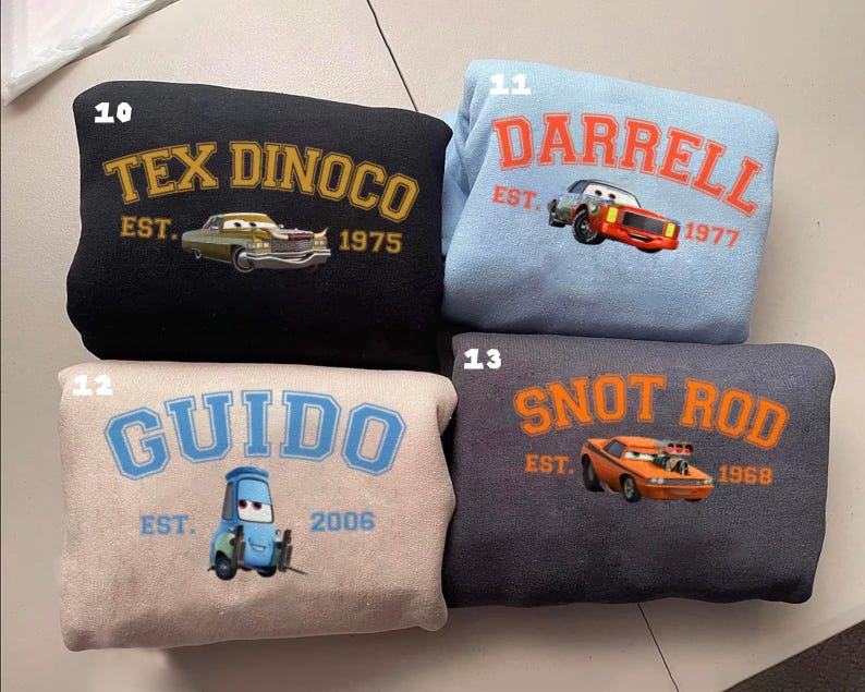 May include: Four sweatshirts with car-themed designs. A black sweatshirt features "TEX DINOCO EST. 1975" with a car graphic. A light blue sweatshirt displays "DARRELL EST. 1977". A beige sweatshirt has "GUIDO EST. 2006". A dark grey sweatshirt shows "SNOT ROD EST. 1968".