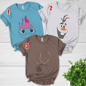 Pu&ograve; includere: Tre magliette a maniche corte con disegni di personaggi dei cartoni animati. Una &egrave; azzurra con un lucertola dei cartoni animati, un'altra &egrave; bianca con la faccia di Olaf e la terza &egrave; marrone con una renna dei cartoni animati.