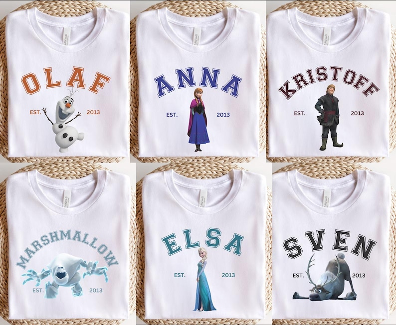 May include: White t-shirts with characters from the film Frozen. Each shirt displays a character's name in a varsity style font, with the year "2013" beneath. Characters include Olaf, Anna, Kristoff, Marshmallow, Elsa, and Sven.