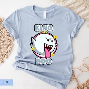Op de afbeelding: Lichtblauw T-shirt met een cartoon afbeelding van King Boo uit de Super Mario-franchise. De afbeelding toont King Boo met een kroon en een roze tong die uitsteekt. De tekst "King Boo" is boven de afbeelding gedrukt.