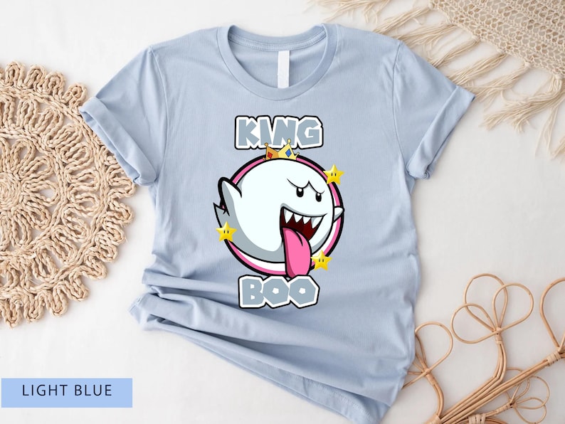 Op de afbeelding: Lichtblauw T-shirt met een cartoon afbeelding van King Boo uit de Super Mario-franchise. De afbeelding toont King Boo met een kroon en een roze tong die uitsteekt. De tekst "King Boo" is boven de afbeelding gedrukt.
