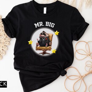 May include: Black t-shirt featuring a cartoon character in a suit, seated in a gold chair, with the words "MR. BIG" above. The design includes three yellow star accents. The word "BLACK" is printed at the bottom.