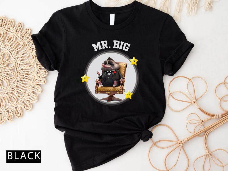 May include: Black t-shirt featuring a cartoon character in a suit, seated in a gold chair, with the words "MR. BIG" above. The design includes three yellow star accents. The word "BLACK" is printed at the bottom.