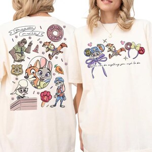 May include: An off-white t-shirt featuring Zootopia character graphics. The back displays a collage of characters, a police badge, a donut, and the text 'You can be whatever you wish to be.' The front shows character-themed ears and the text 'You can be anything you wish to be.'