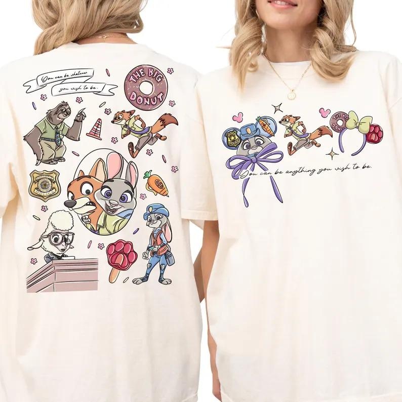 May include: An off-white t-shirt featuring Zootopia character graphics. The back displays a collage of characters, a police badge, a donut, and the text 'You can be whatever you wish to be.' The front shows character-themed ears and the text 'You can be anything you wish to be.'