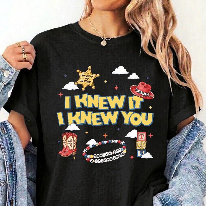 Puede incluir: Una camiseta negra con un estampado gr&aacute;fico que incluye el texto I KNEW IT I KNEW YOU, una estrella de sheriff amarilla, un sombrero de vaquero rojo, botas de vaquero rojas, una pulsera de cuentas colorida con texto y tres cubos apilados.