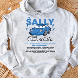 May include: A light gray hooded sweatshirt featuring a blue cartoon car with the text "I'm SALLY". The design includes lightning bolts and the phrase "I'M LIGHTING!". Additional text describes the car's character.