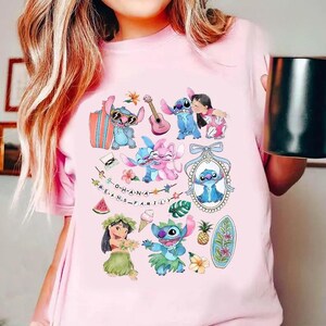 Może przedstawiać: Jasnor&oacute;żowy t-shirt z kolorowym nadrukiem graficznym przedstawiającym postać Stitcha i Lilo. Wz&oacute;r zawiera r&oacute;żne ilustracje, takie jak deska surfingowa, ukulele, tropikalne kwiaty, ananas oraz napis O-H-A-N-A M-E-A-N-S F-A-M-I-L-Y.