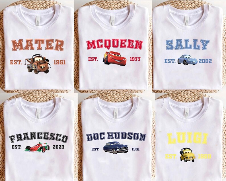 May include: White t-shirts with designs from the film Cars. Each shirt displays a character's name, such as "Mater" or "McQueen," alongside a car graphic and the year of establishment. The designs are in various colours.