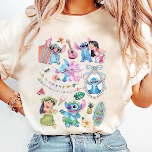 Może przedstawiać: Kremowy t-shirt z nadrukiem graficznym przedstawiającym postacie Stitcha i Lilo, deskę surfingową, gitarę, ananasa, kawałek arbuza, rożek lodowy oraz sznur lampek z napisem O-H-A-N-A M-E-A-N-S F-A-M-I-L-Y.