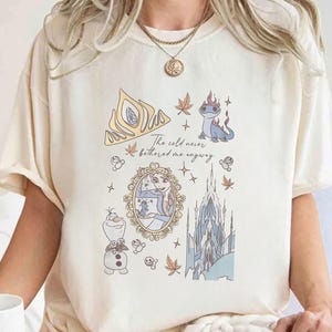 Puede incluir: Camiseta color crema con un dise&ntilde;o de dibujos animados con elementos de la pel&iacute;cula Frozen. El dise&ntilde;o incluye una corona dorada, Elsa, Olaf, un castillo y el texto "The cold never bothered me anyway."