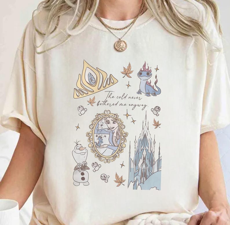 Puede incluir: Camiseta color crema con un dise&ntilde;o de dibujos animados con elementos de la pel&iacute;cula Frozen. El dise&ntilde;o incluye una corona dorada, Elsa, Olaf, un castillo y el texto "The cold never bothered me anyway."